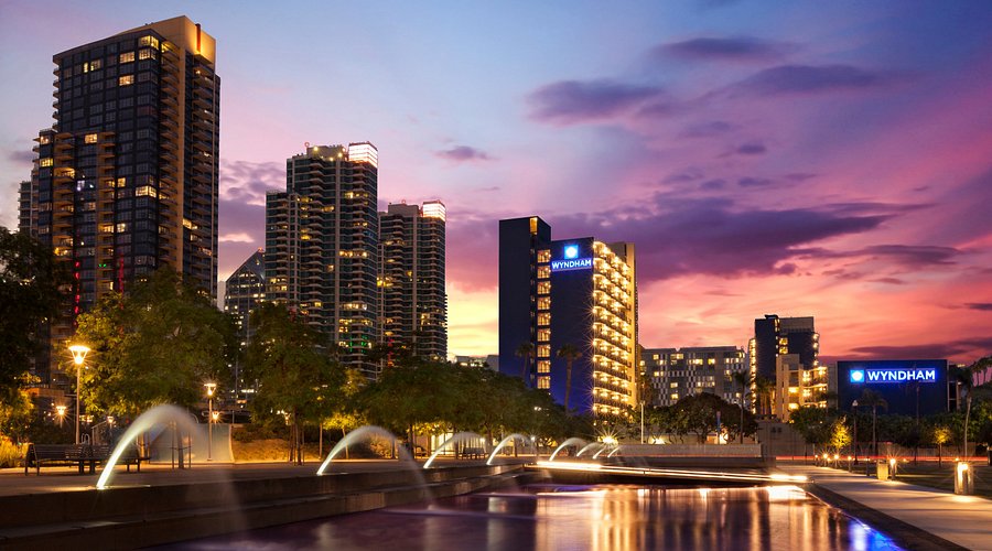 A city skyline at dusk featuring illuminated buildings and water fountains